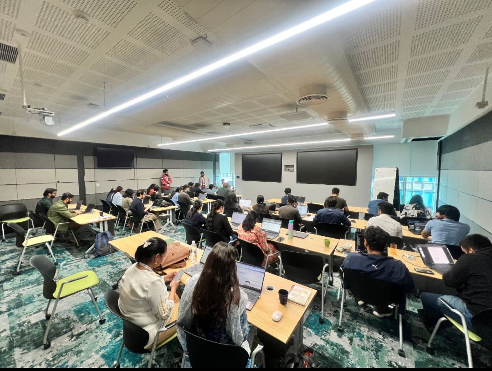 Classroom-style AI training with participants at laptops in a modern corporate learning centre