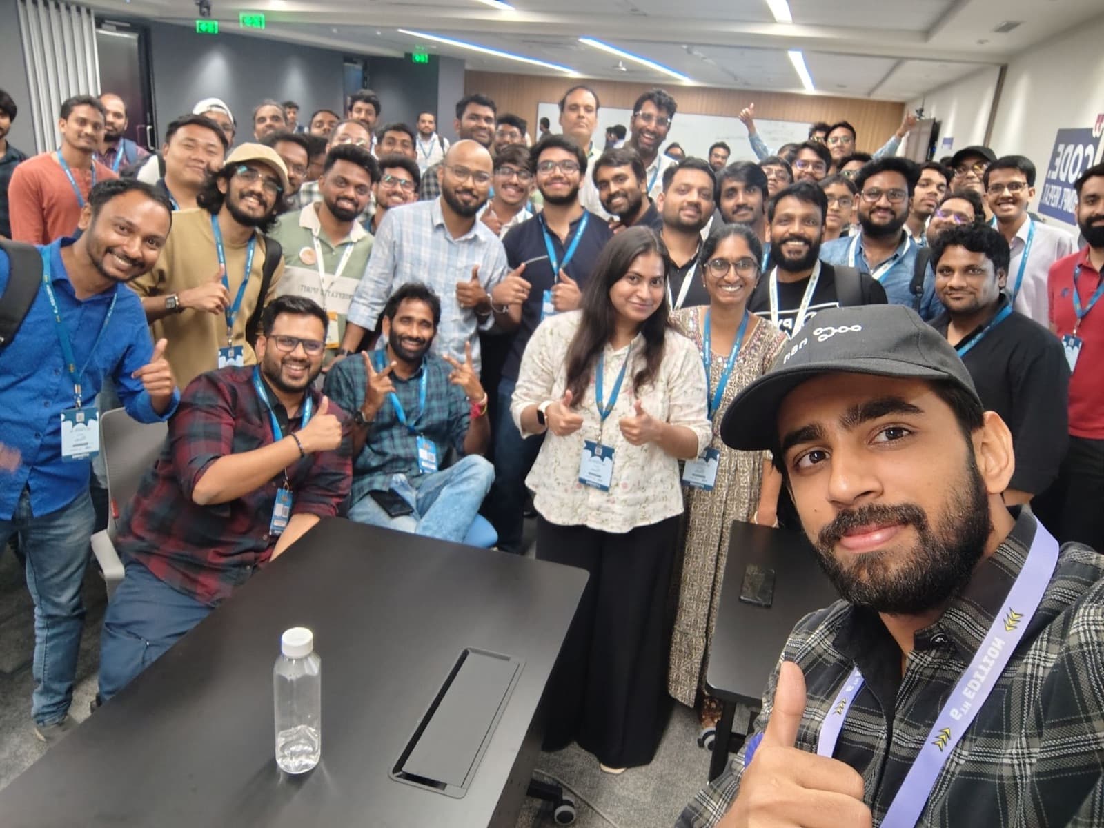 Large group of workshop participants with lanyards giving thumbs-up in a selfie